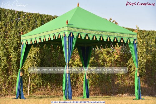 Green canopy tent with blue accents and decorative tassels set in a grassy outdoor area.